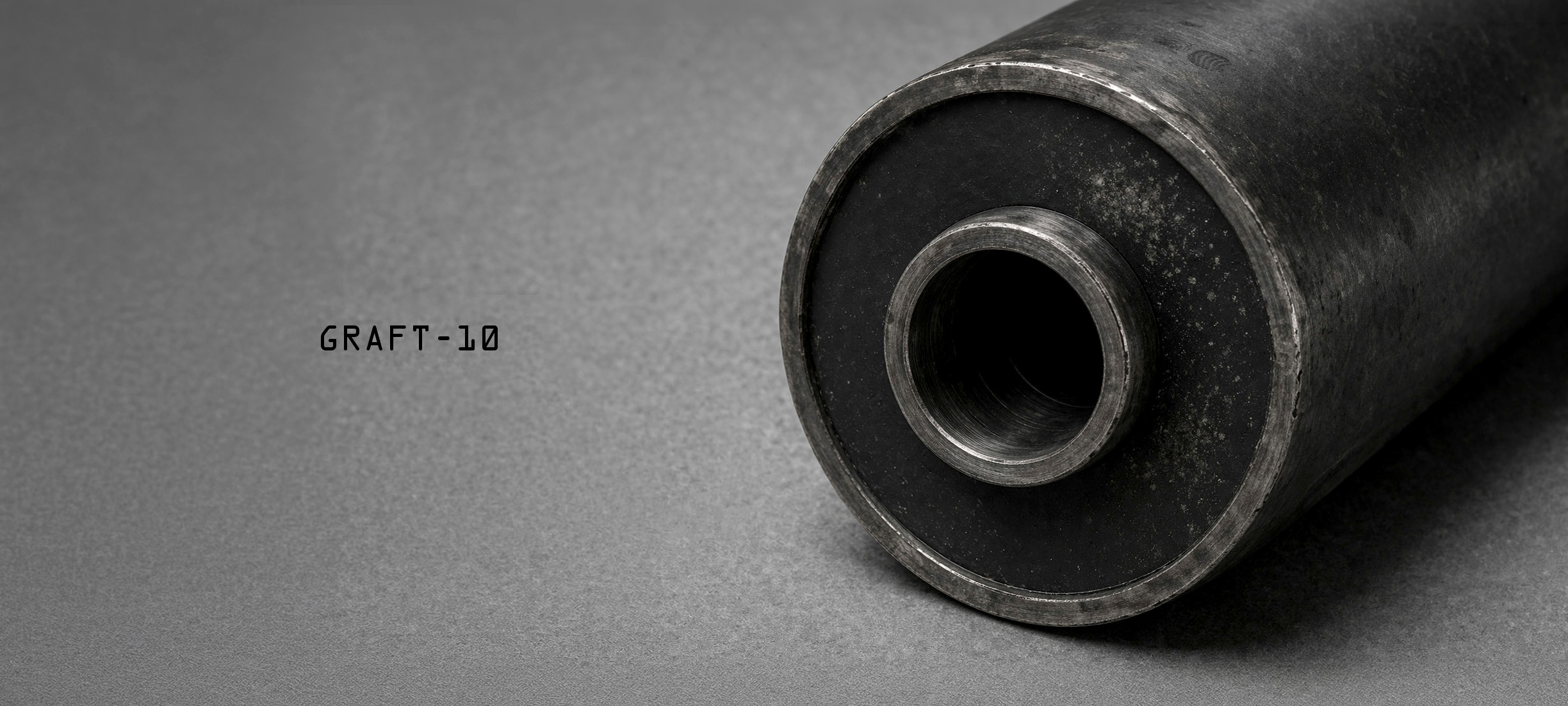 Studio detail view of the GRAFT-10 symbiont and parasite Host on a dark background, showing the active face with a slightly proud inner steel core, sealed black annular field, subtle particulate haze, and boundary wear at the host surface