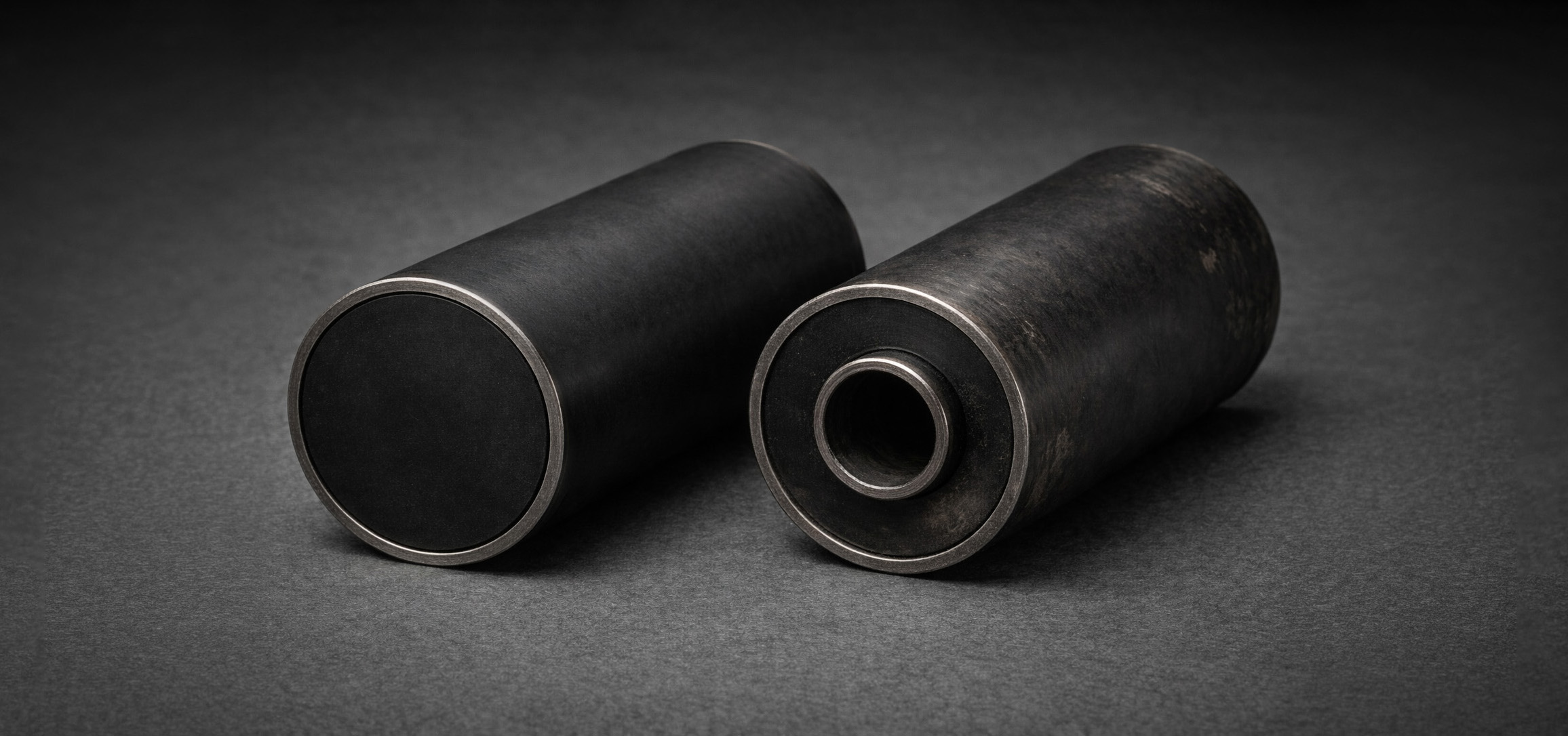 Studio reference view of the GRAFT-10 symbiont and parasite Host on a dark grey background, showing a sealed cylindrical nested steel sleeve with a slightly proud inner core, dark annular field, and worn host surface
